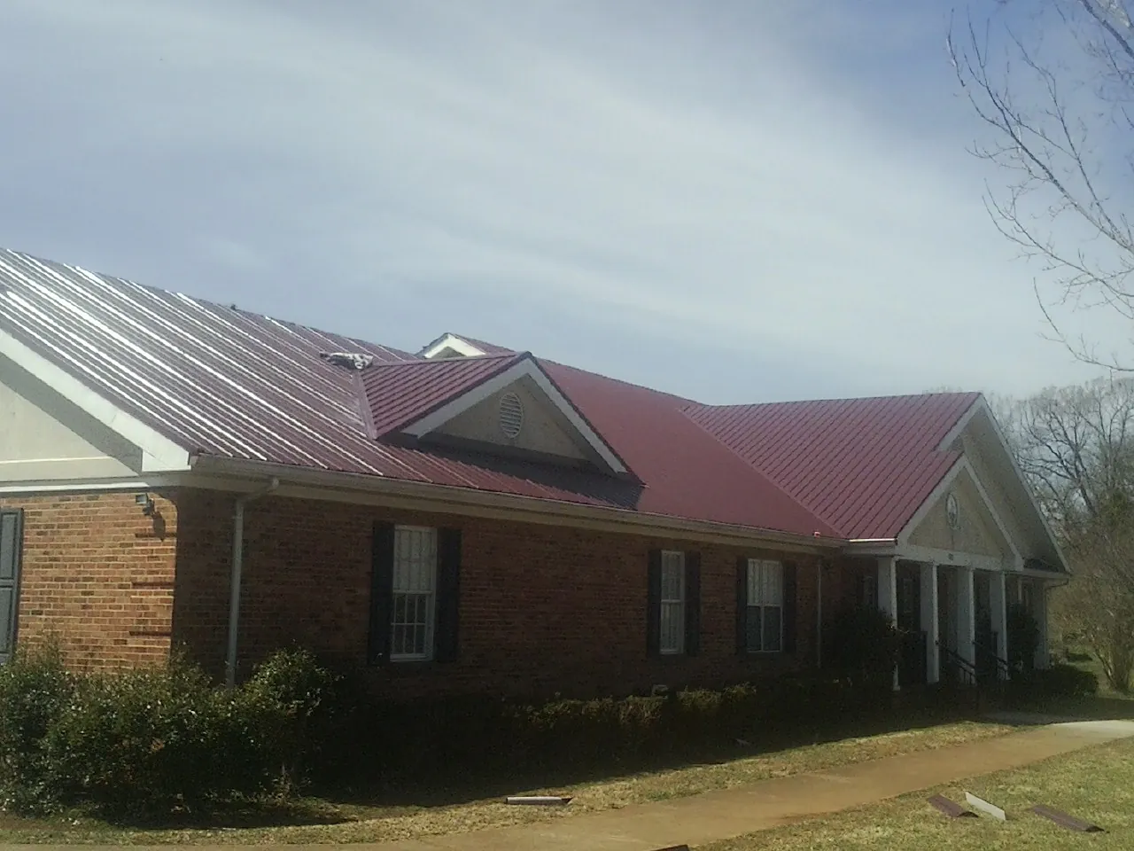 Red metal roof with gabled entries on a long brick building, from a Hail Damage Roof Repair job in Sugarcreek