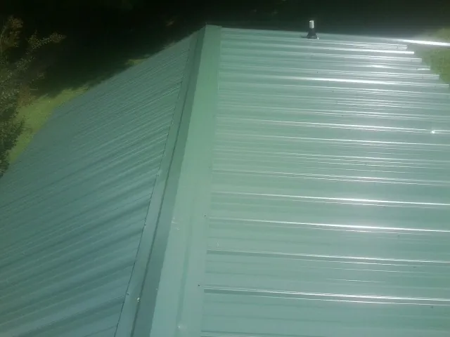 New green metal panels meeting at the ridge of a roof — Flat Roof Repair work by our crew in Sugarcreek