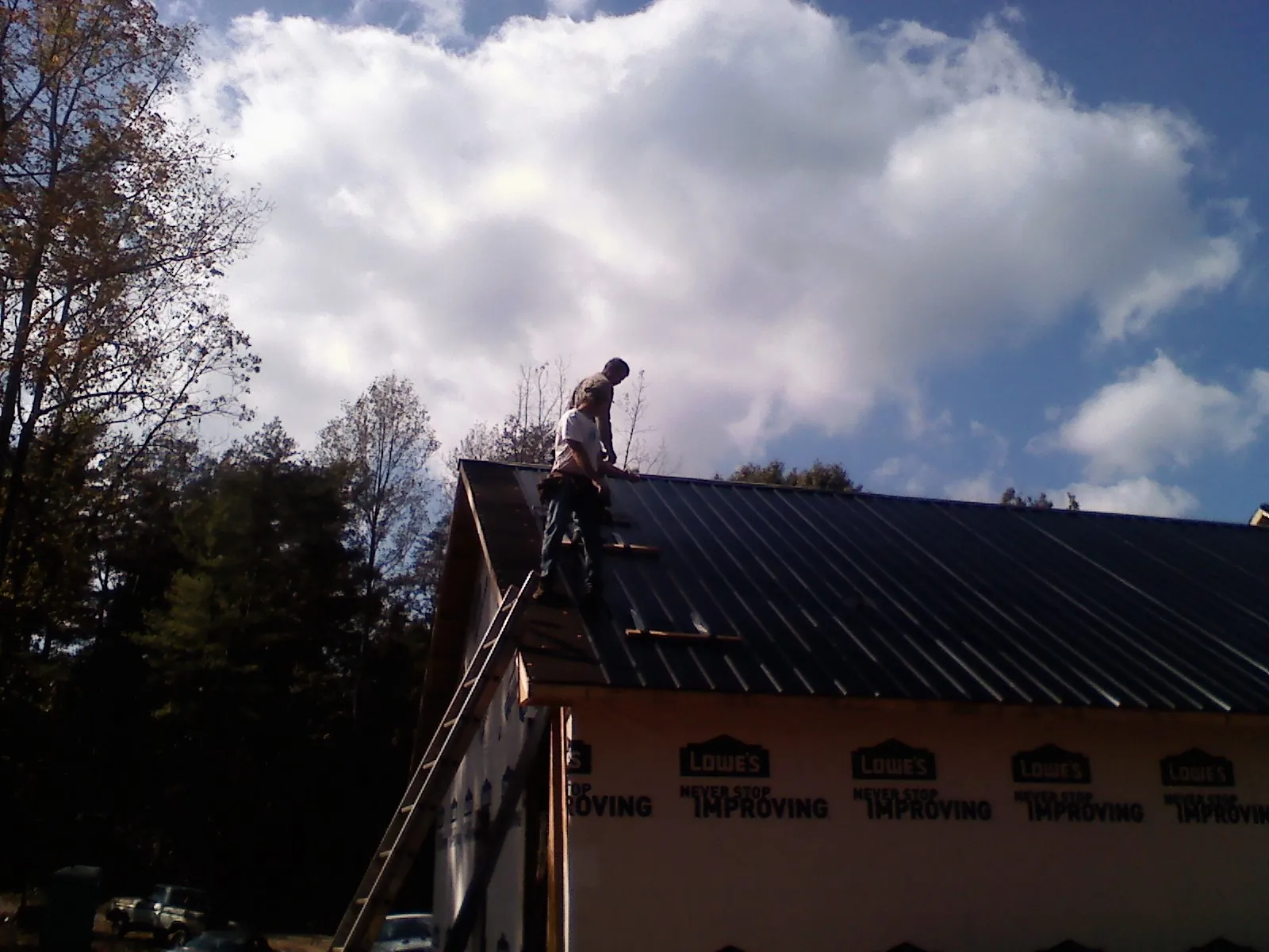 Roofer fastening dark metal panels high against a cloudy sky, from a Roof Inspection job in Sugarcreek