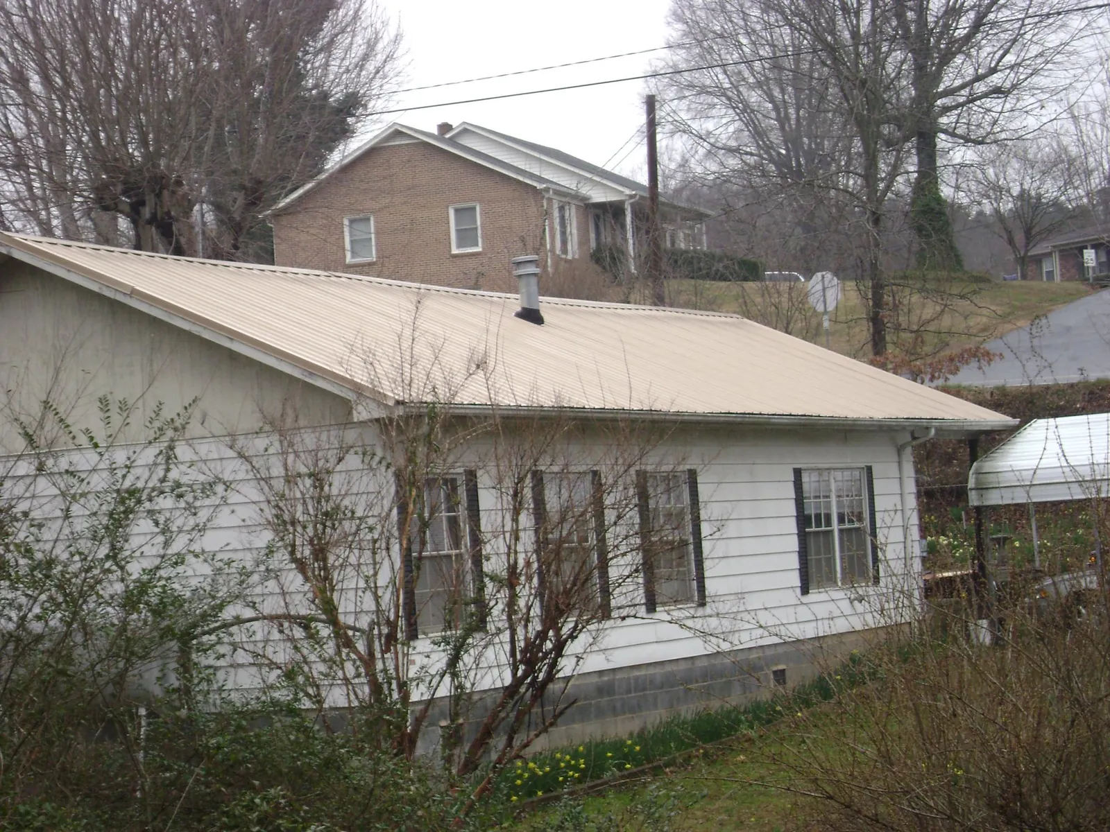 Tan metal roof on a white sided house set into a hillside — Commercial Roofing by Roofing Brothers in Sugarcreek