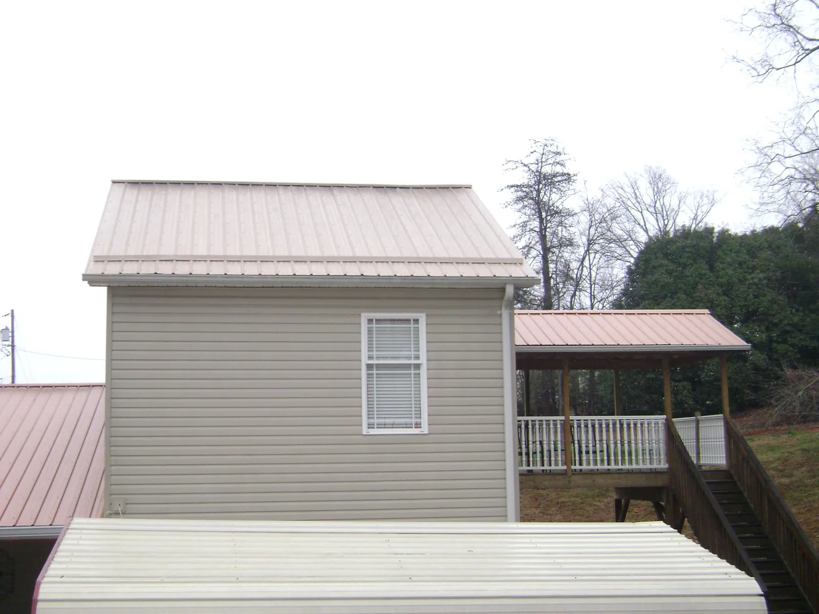Tan metal roofs on a two story addition and attached porch, from a Roof Replacement job in Sugarcreek